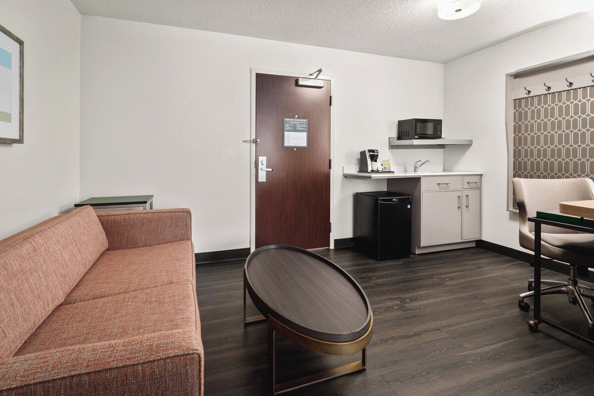 Een moderne hotelkamer met een bank, een klein rond tafeltje, een magnetron, een spoelbak en een kast.