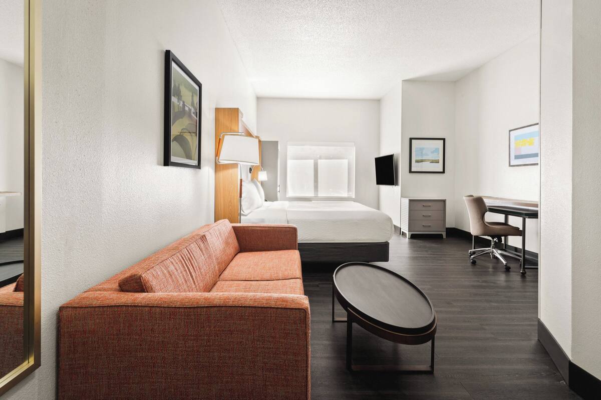 A modern hotel room with a sofa, a desk, a bed, and a chair.