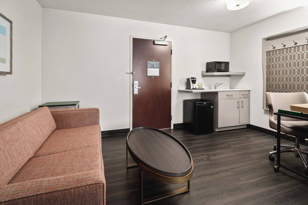 A modern hotel room with a sofa, a small round table, a microwave, a sink, and a cabinet.