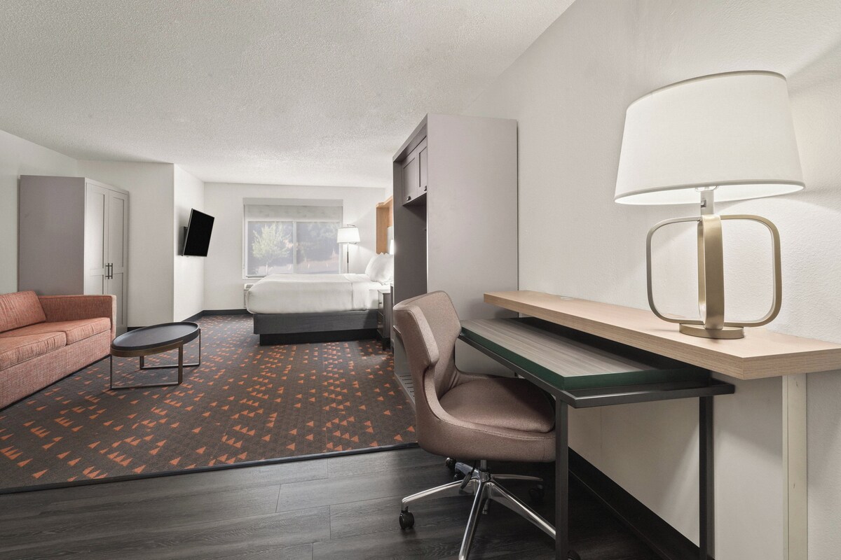 Een hotelkamer met een bed, een bureau met een lamp, een bank en een televisie aan de muur.