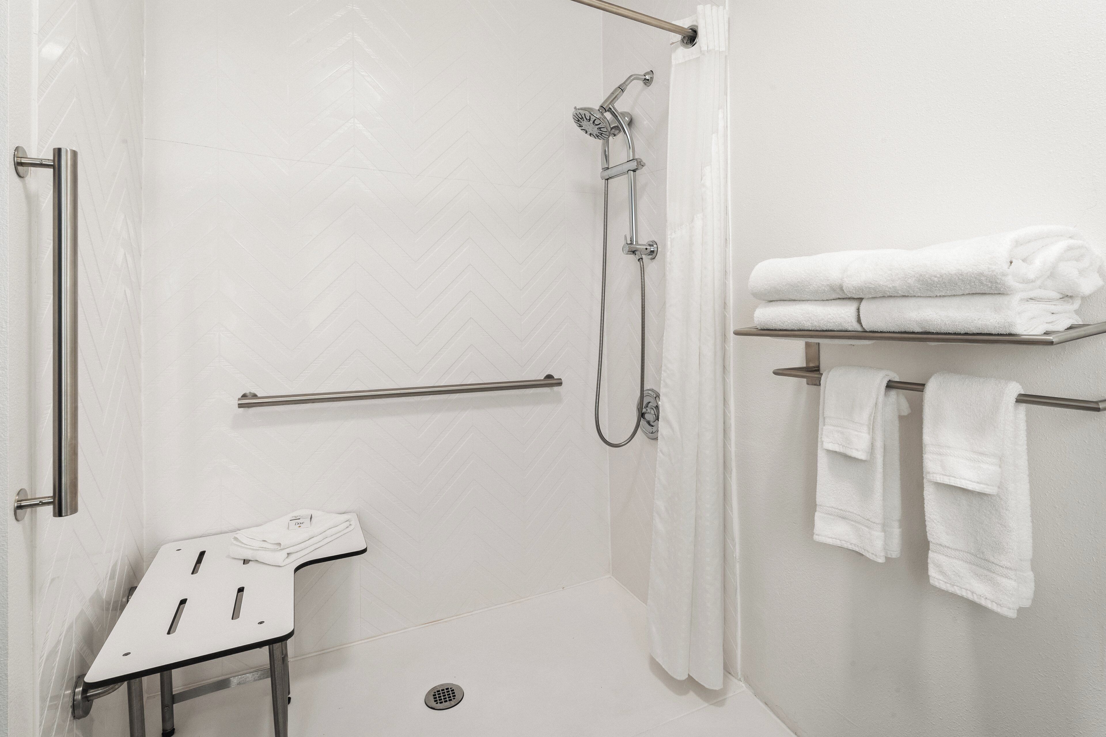 Un espace douche équipé d’un pommeau de douche à main, d’une barre d’appui et d’un porte-serviettes avec des serviettes pliées.