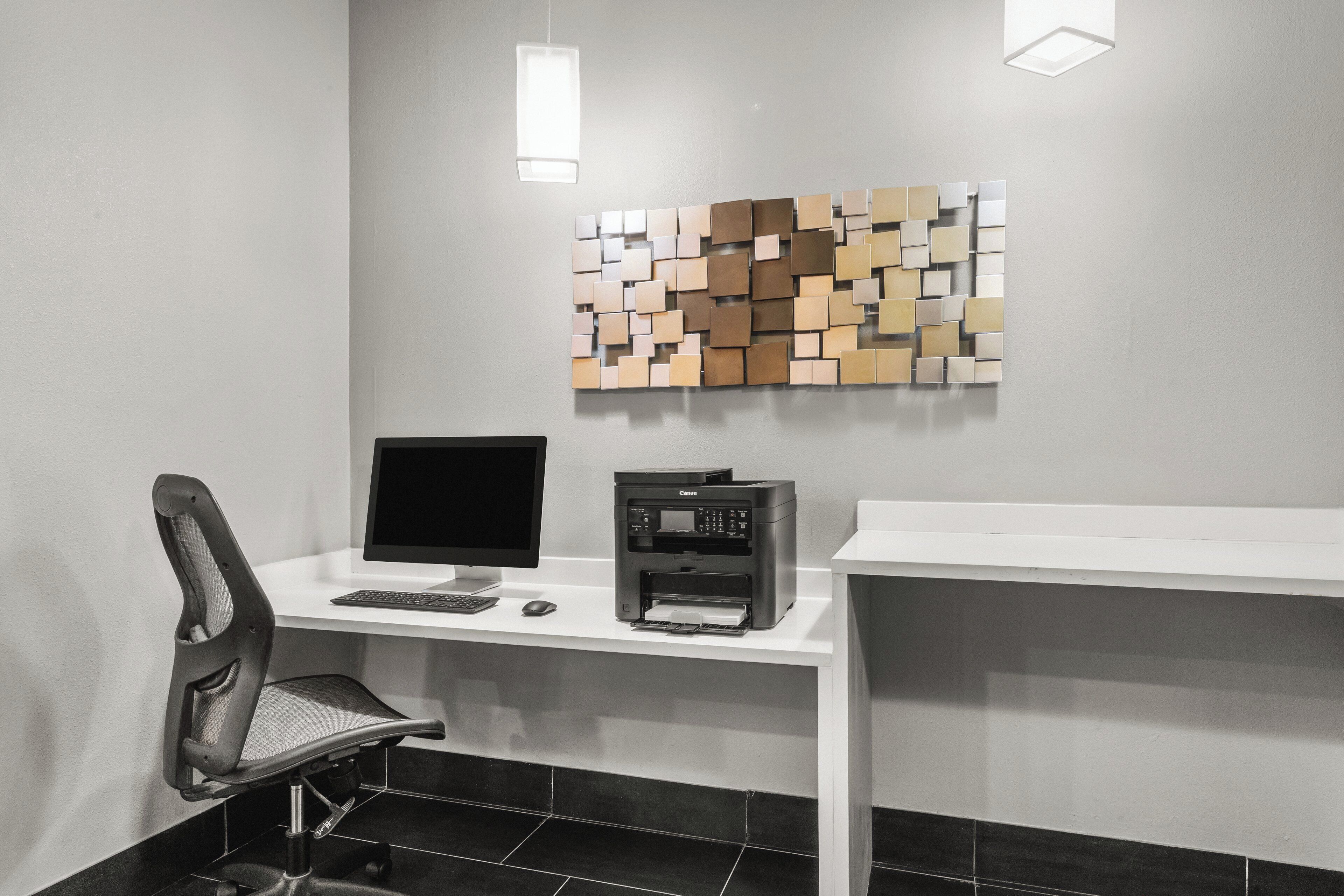 Ein moderner Arbeitsraum mit Schreibtisch, Stuhl, Computermonitor, Drucker und einem an der Wand befestigten abstrakten Kunstwerk.
