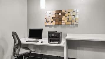 Um espaço de escritório moderno com mesa, cadeira, monitor de computador, impressora e uma obra de arte abstrata na parede.