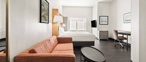 A hotel room with a bed, a sofa, a desk, and a chair.