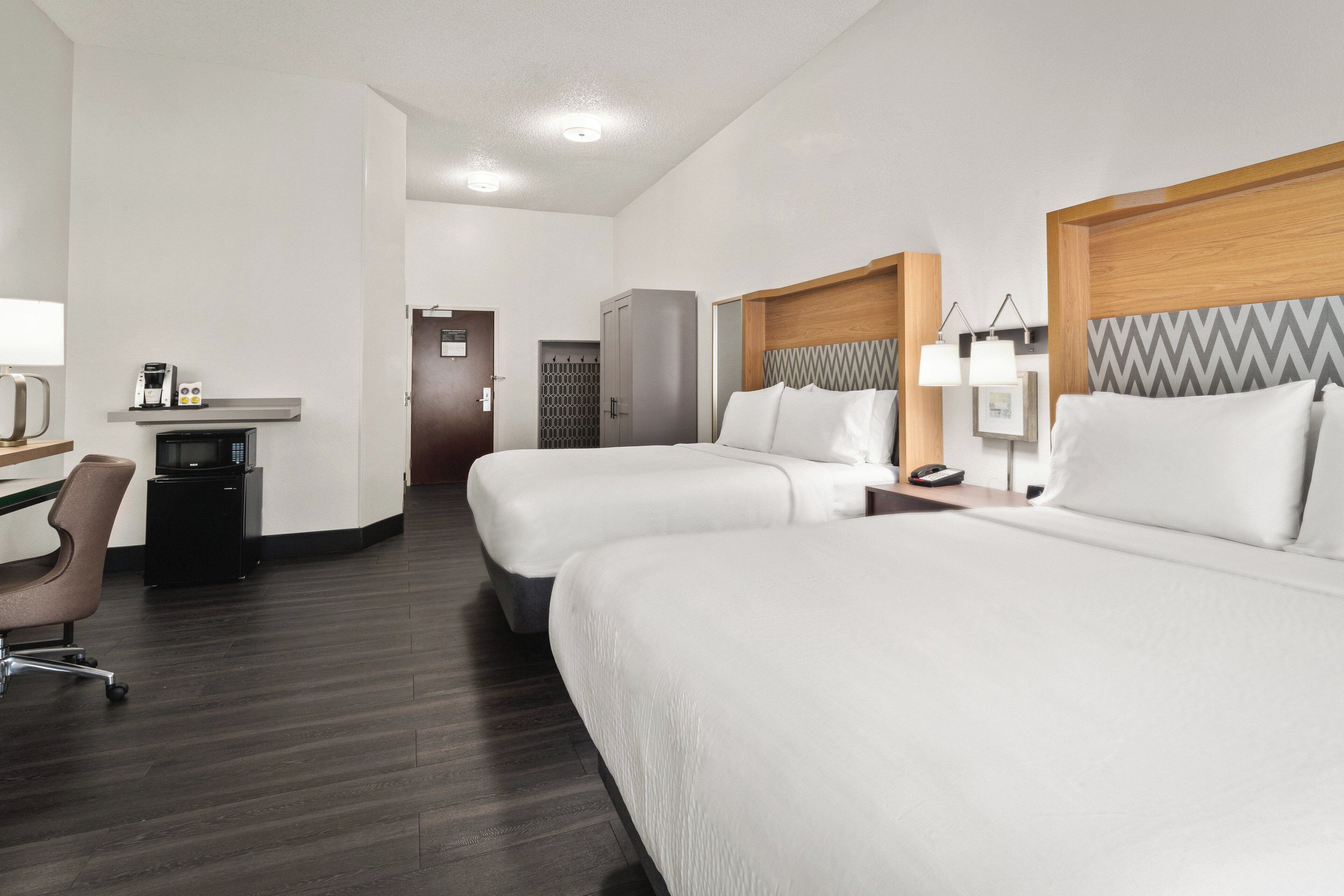Une chambre d’hôtel avec deux lits, un bureau avec une chaise, un minibar et une télévision.