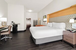 Habitación de hotel con cama, mesita de noche, escritorio, silla y microondas.