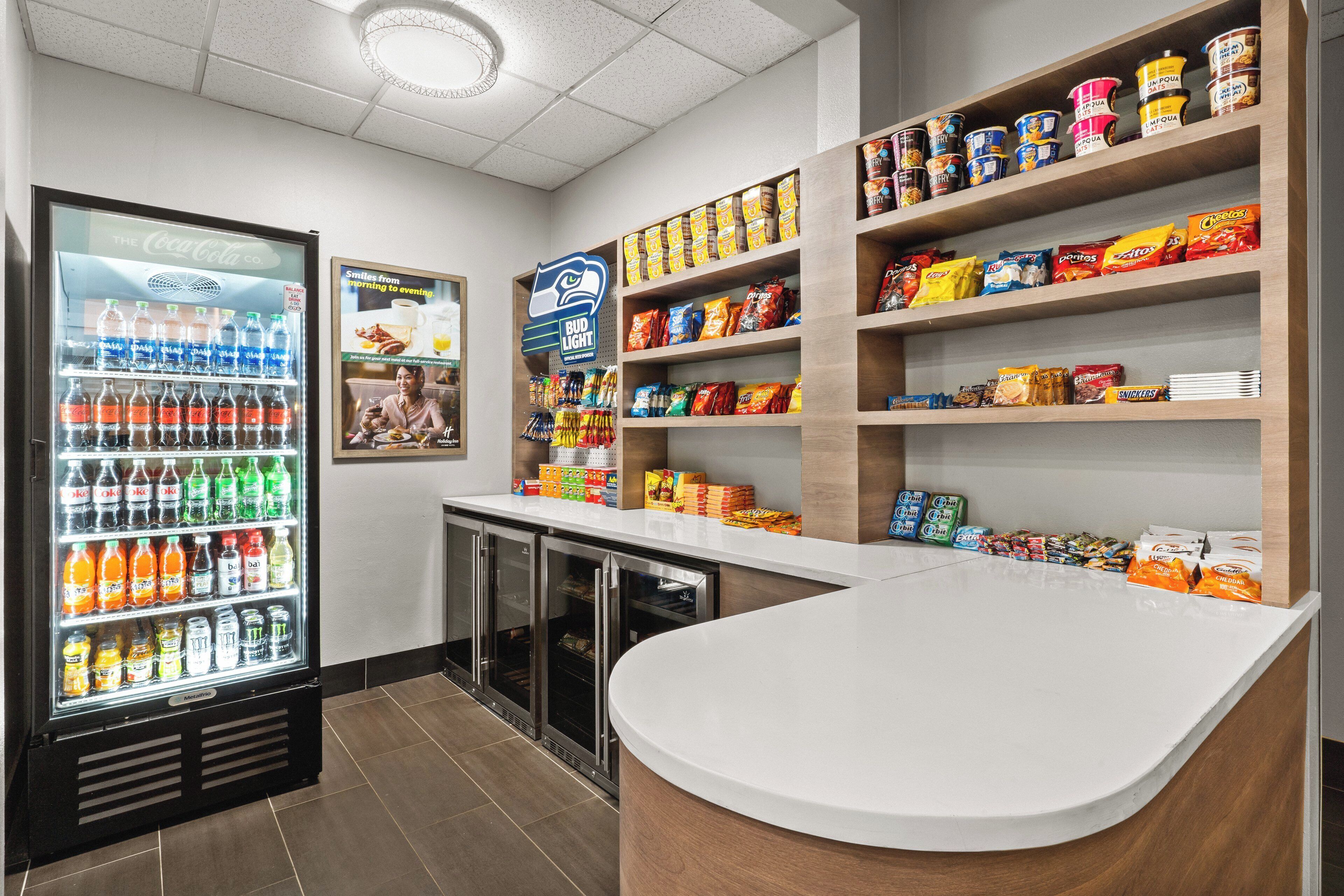 Un bar de aperitivos con refrigerador de Coca-Cola, cartel de Bud Light y estantes repletos de bocadillos y bebidas.