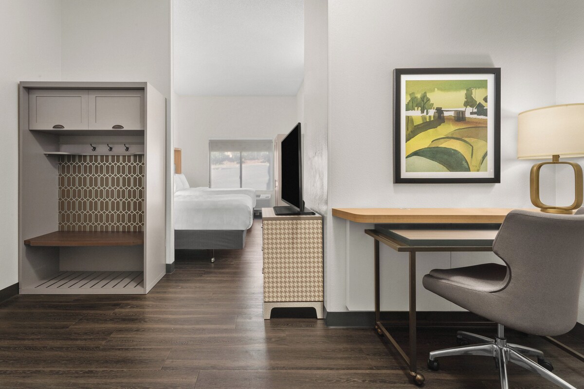Een hotelkamer met een bed, een bureau met stoel, een televisie en een schilderij aan de muur.