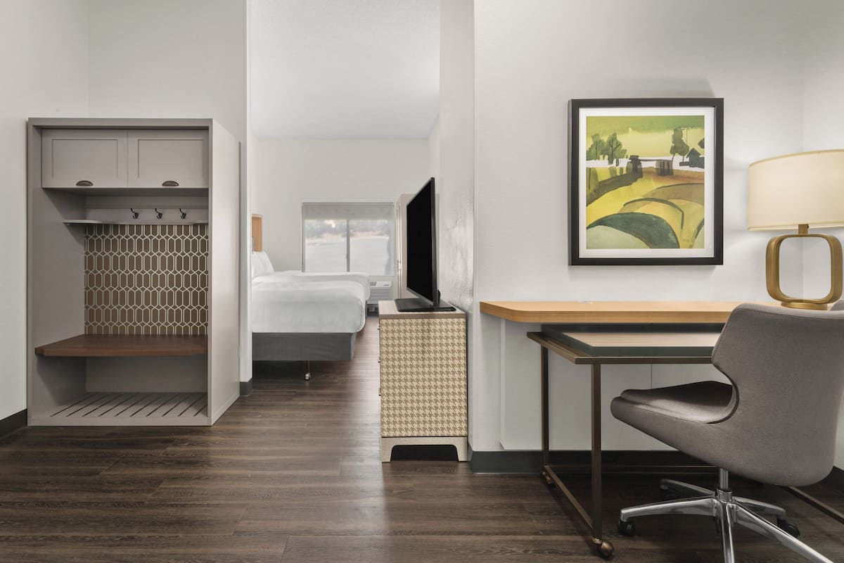 A hotel room with a bed, a desk with a chair, a television, and a painting on the wall.