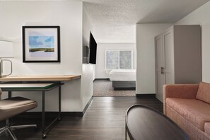 A modern hotel room with a desk, chair, bed, and a sofa.