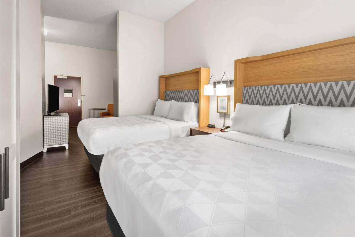 A hotel room with two beds, a television, a desk, and a chair.