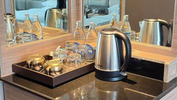 A hotel room's minibar with a tea kettle, glass bottles, and a tray with cups and glasses.