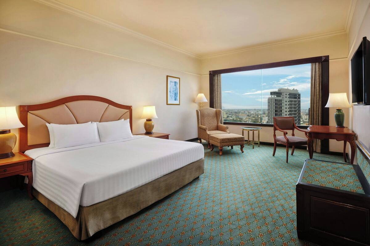 A hotel room with a large bed, two chairs, a small table, and a TV.