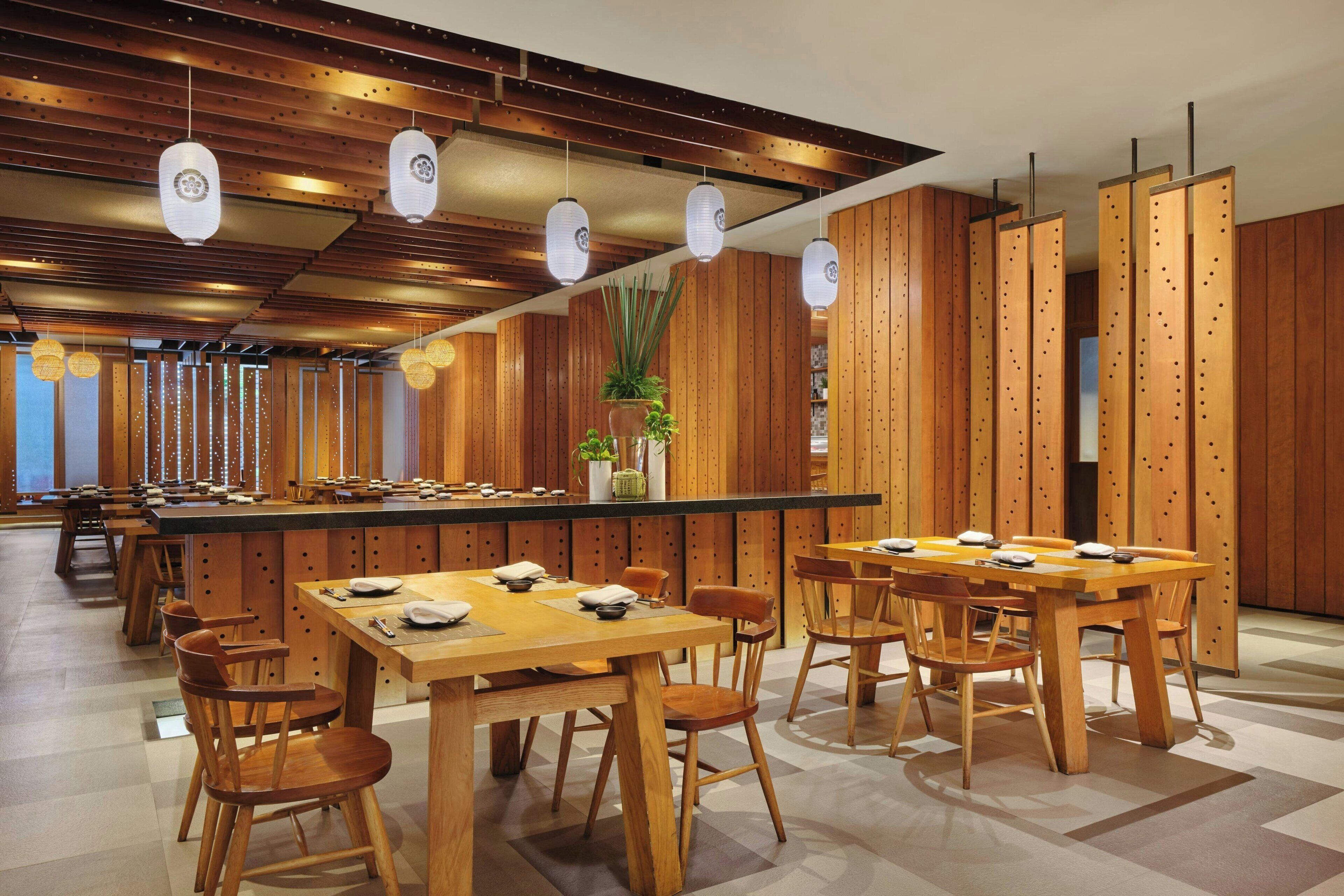 Un restaurante con mesas y sillas de madera, una barra con una planta y faroles colgantes.