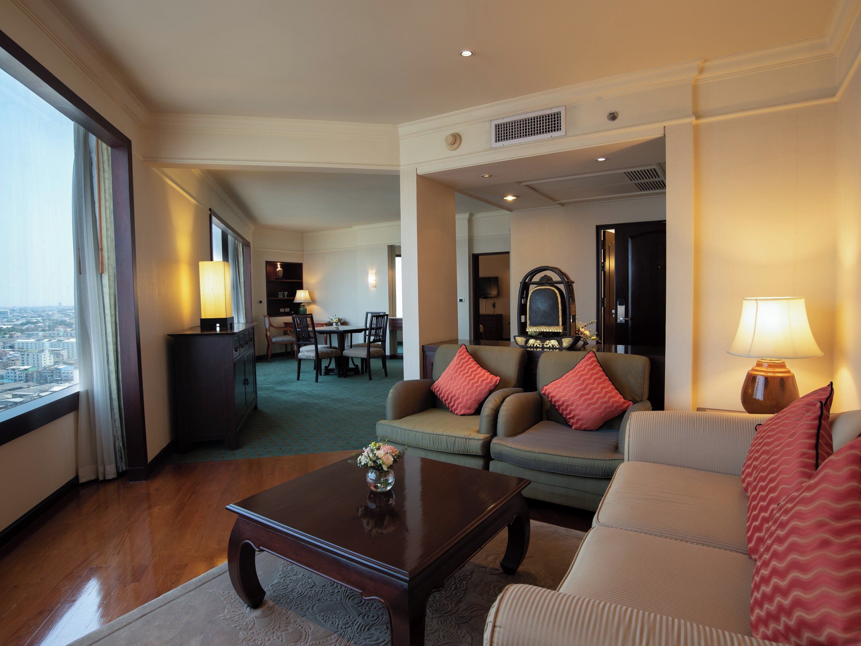 A hotel room with a living area featuring a sofa, armchairs, a coffee table, and a dining area with a table and chairs.