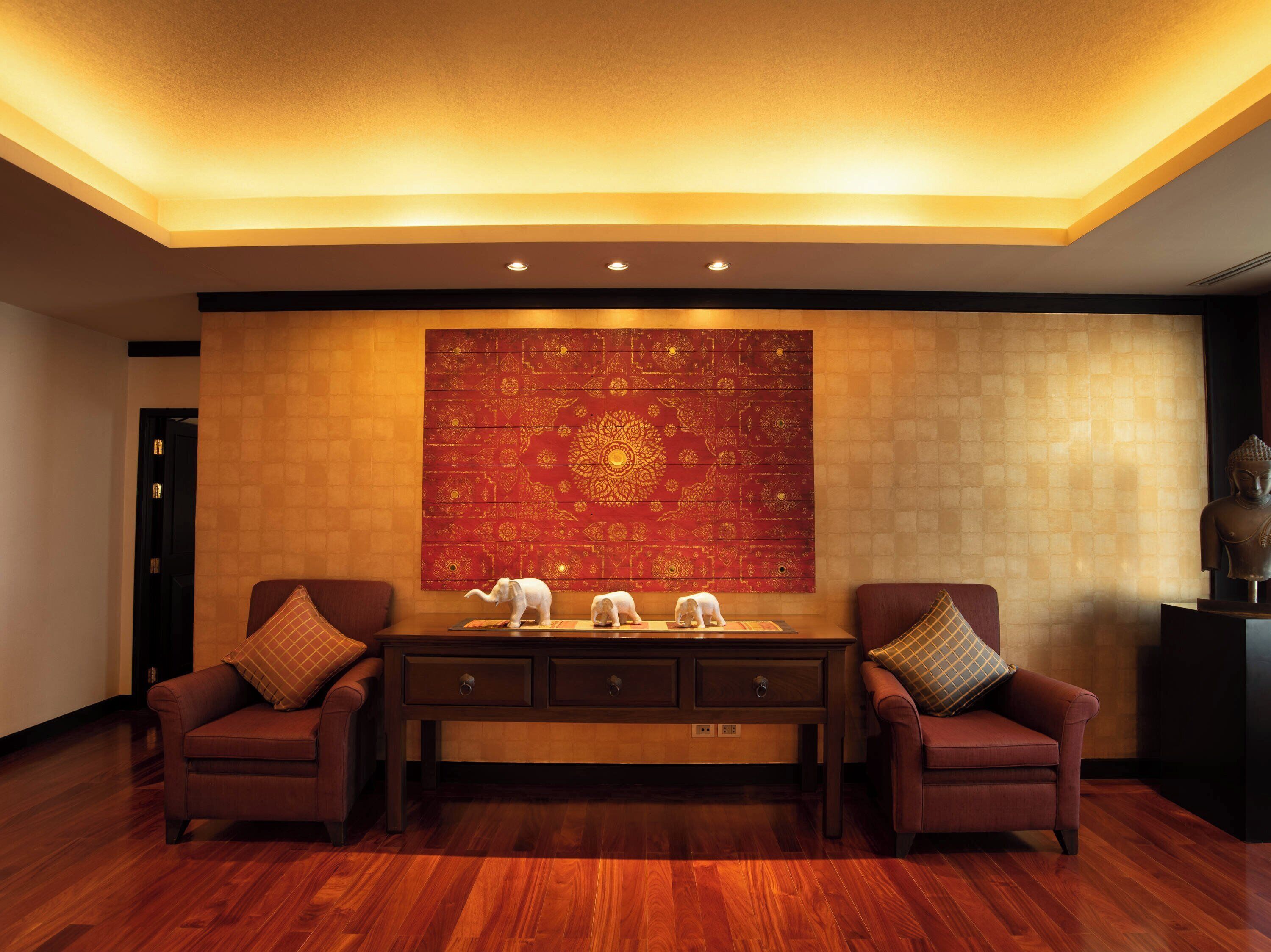 A room with a wooden floor, two armchairs, a central table, and a large tapestry on the wall.