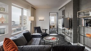 A modern hotel room with a sofa, armchair, coffee table, TV, and a bookshelf. - Swissotel Sydney (Sydney)