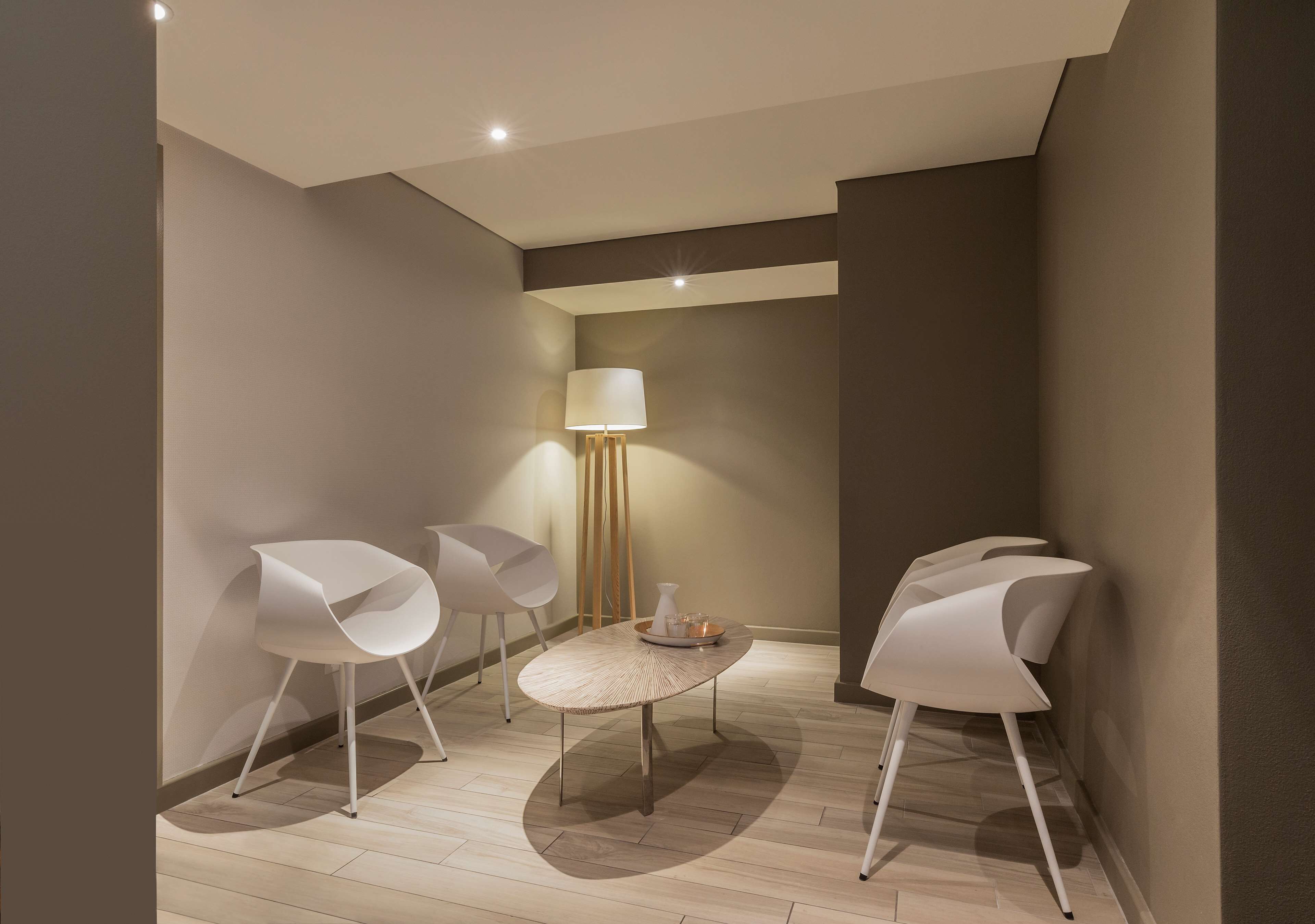 A modern room with a round table, three white chairs, a floor lamp, and a vase with flowers.