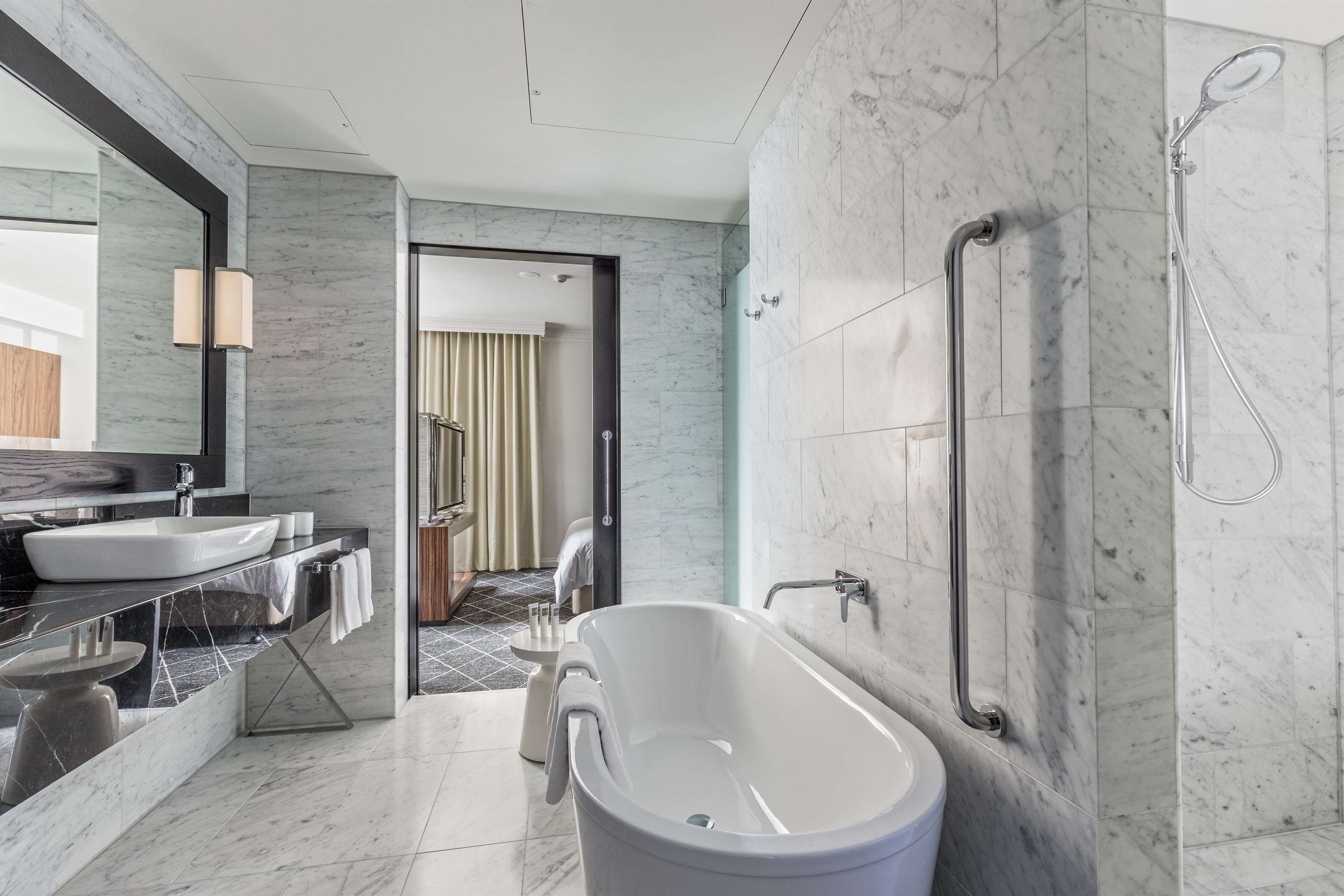 Un baño moderno con una bañera independiente, un tocador con un espejo grande y una ducha con cabezal de ducha manual.