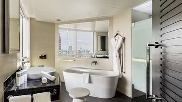 A modern bathroom with a bathtub, two sinks, and a large window offering a city view.