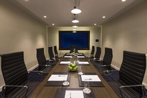 Una sala conferenze con un lungo tavolo, sedie nere, uno schermo per proiettore e una ciotola di frutta sul tavolo.