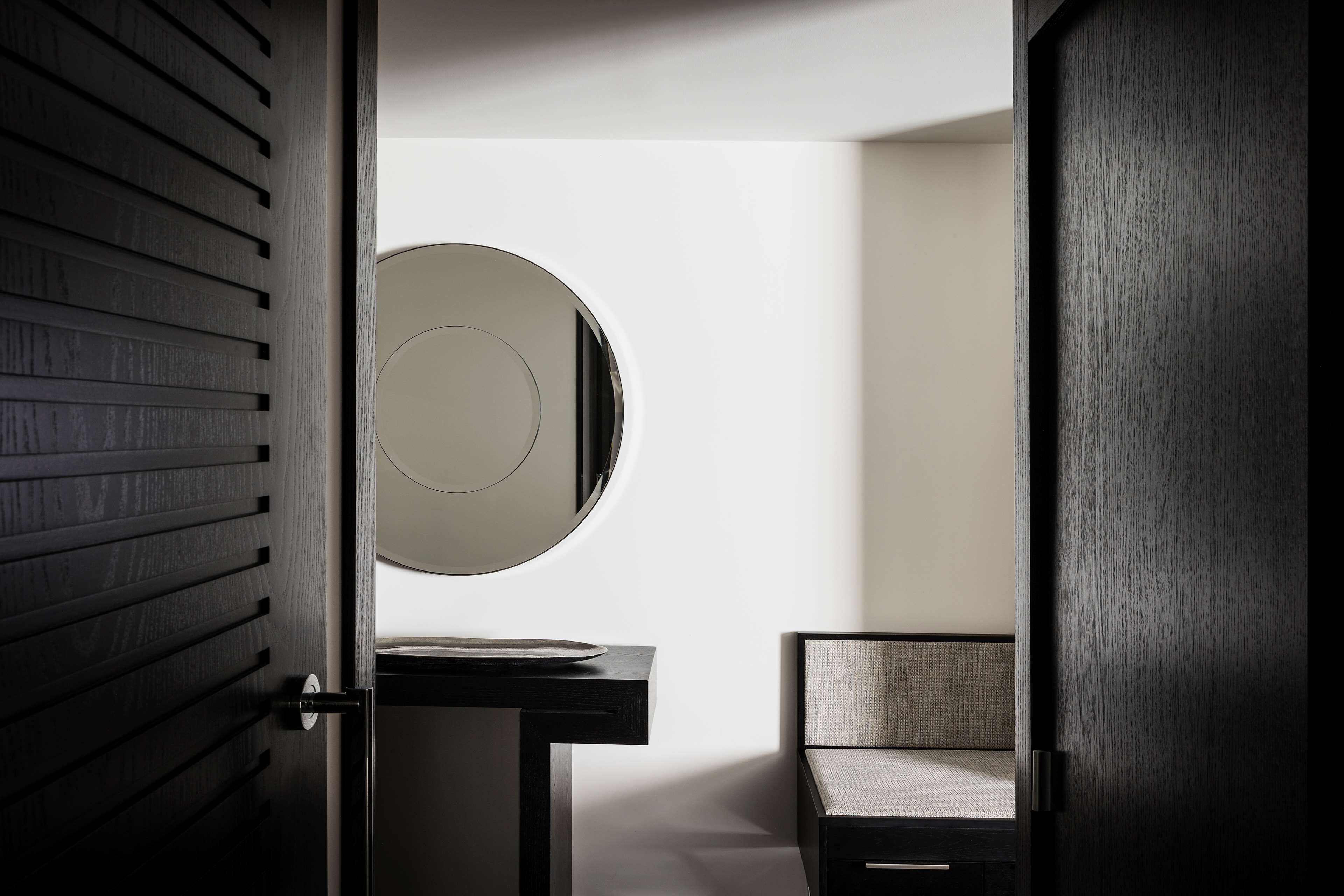 A modern bathroom with a round mirror, a dark wooden door, and a light-colored wall.