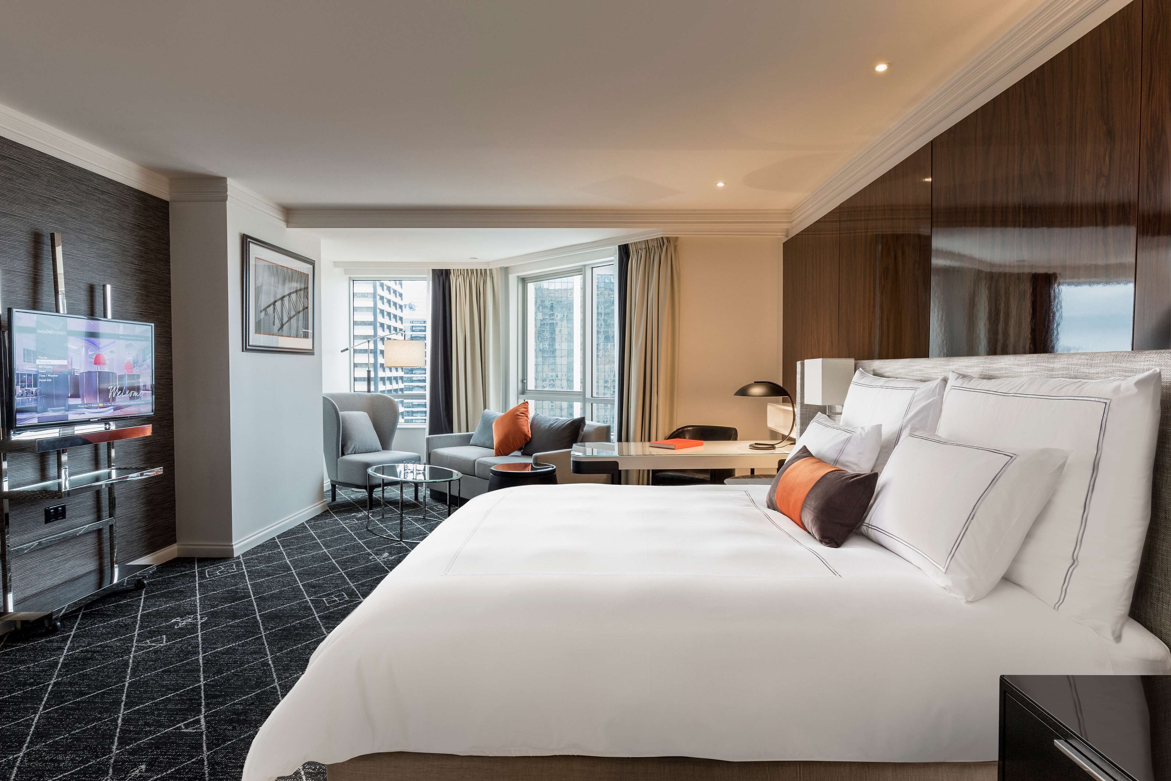 A hotel room with a large bed, a desk, a chair, a TV, and a window with curtains.