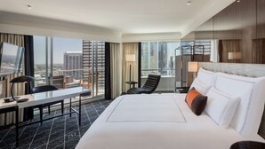 A hotel room with a large bed, a desk, a chair, and a TV. The room has large windows with a city view. - Swissotel Sydney (Sydney)