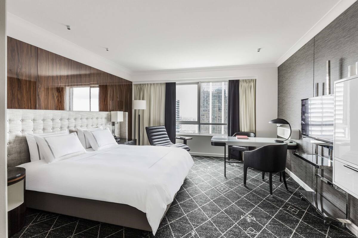 Habitación de hotel moderna con una cama grande, un escritorio, una silla, un televisor y vistas a la ciudad.