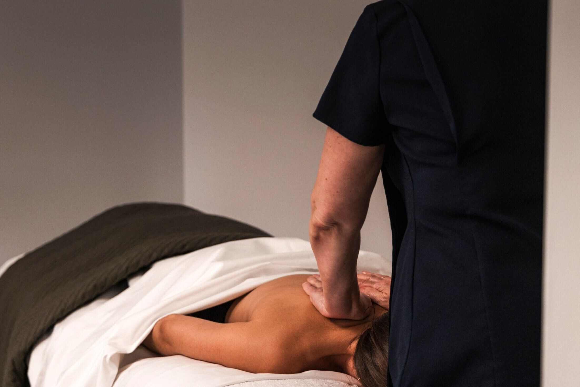 Iemand ontvangt een rugmassage in een kamer met een effen muur en een witte handdoek.
