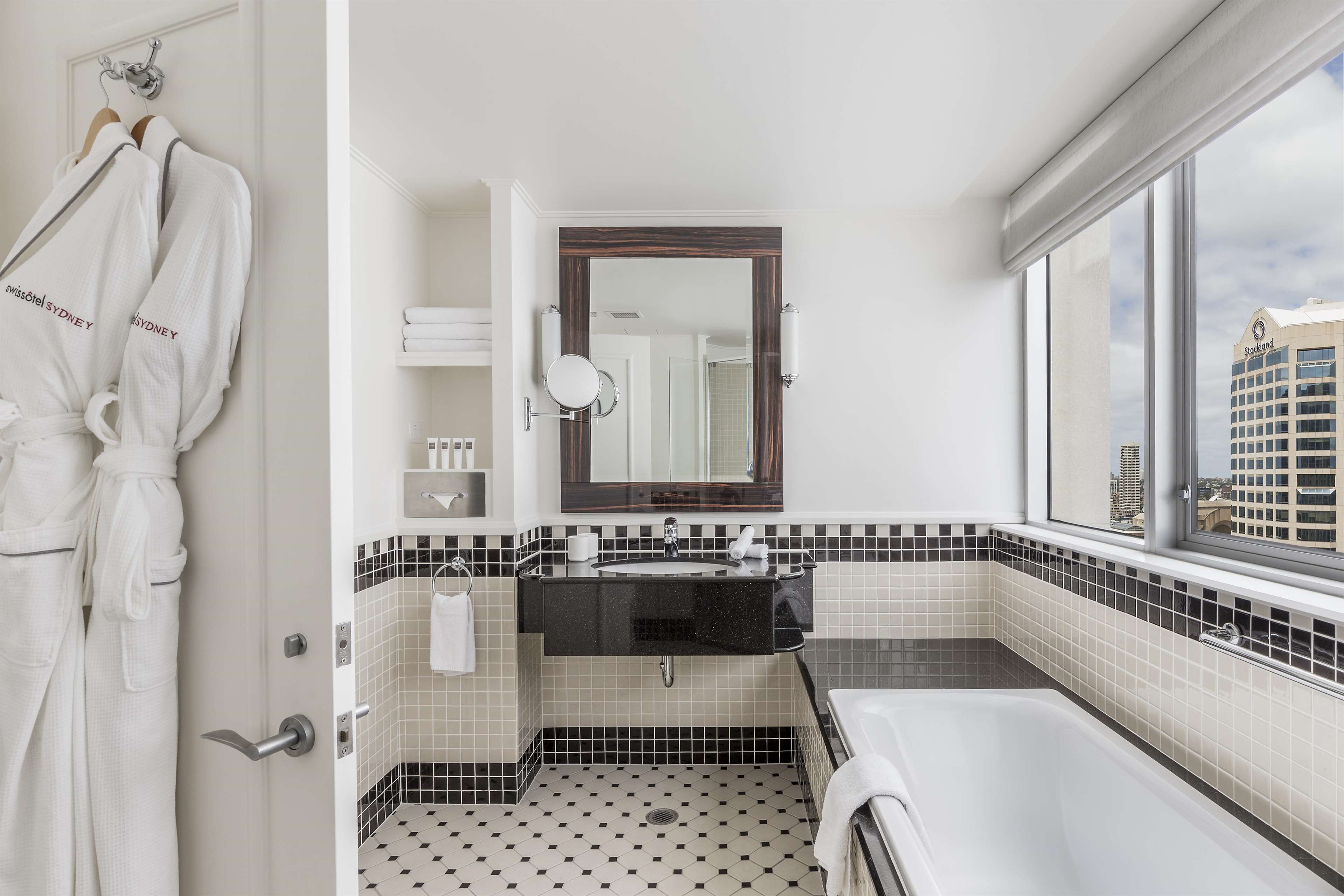Un baño moderno con suelo de baldosas blanco y negro, un espejo grande, un lavabo negro y una bañera.