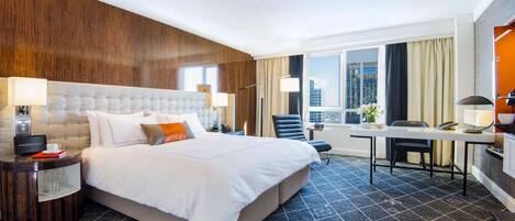 A hotel room with a large bed, a desk, and a view of the city.
