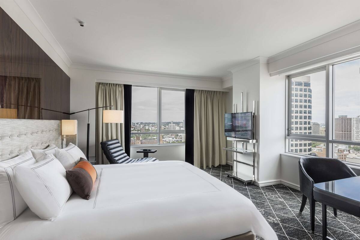 Habitación de hotel con una cama grande, televisión, escritorio y vista a la ciudad.