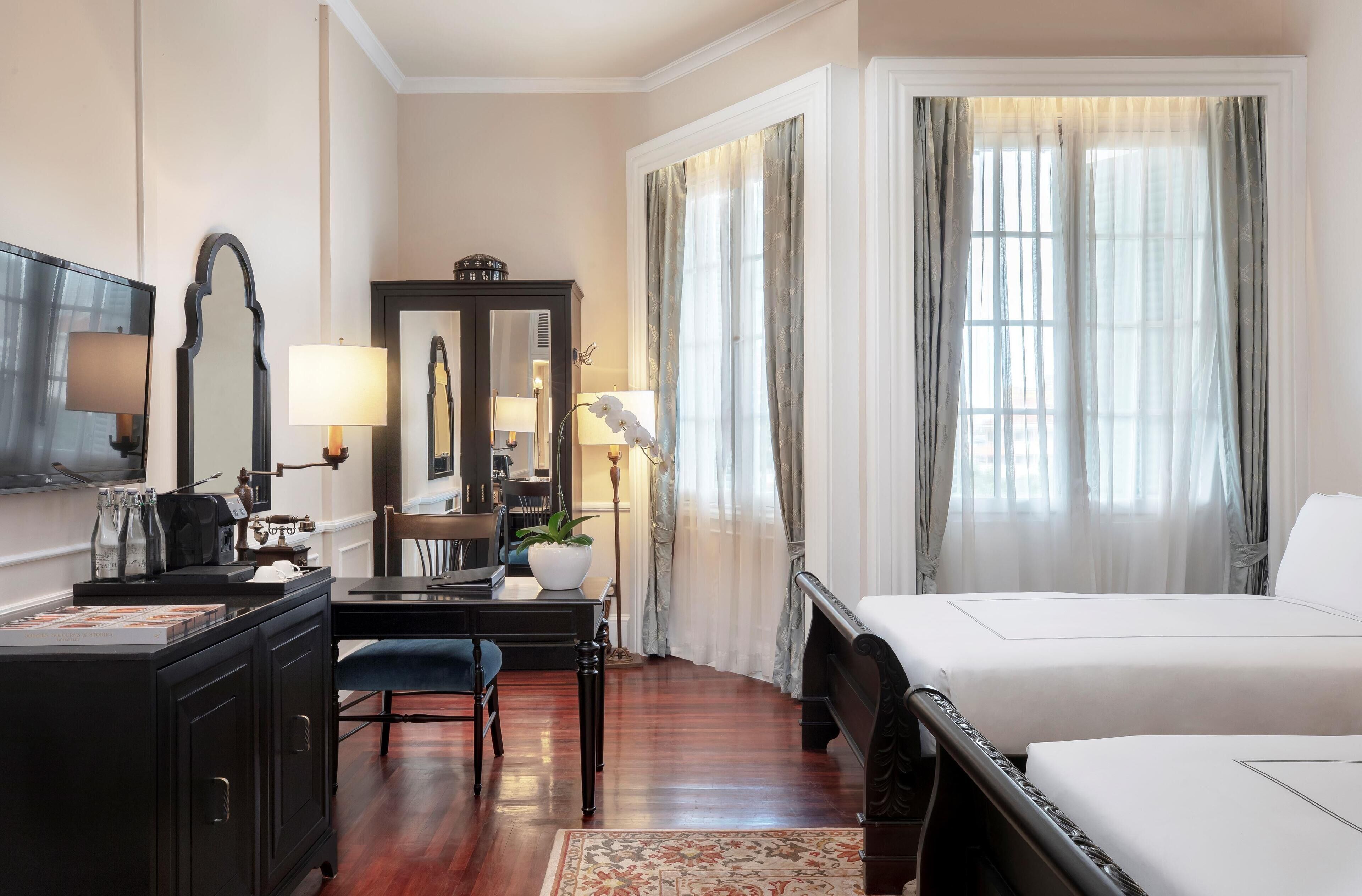 A hotel room with a bed, a desk with a lamp, a chair, a dresser, and a large mirror.