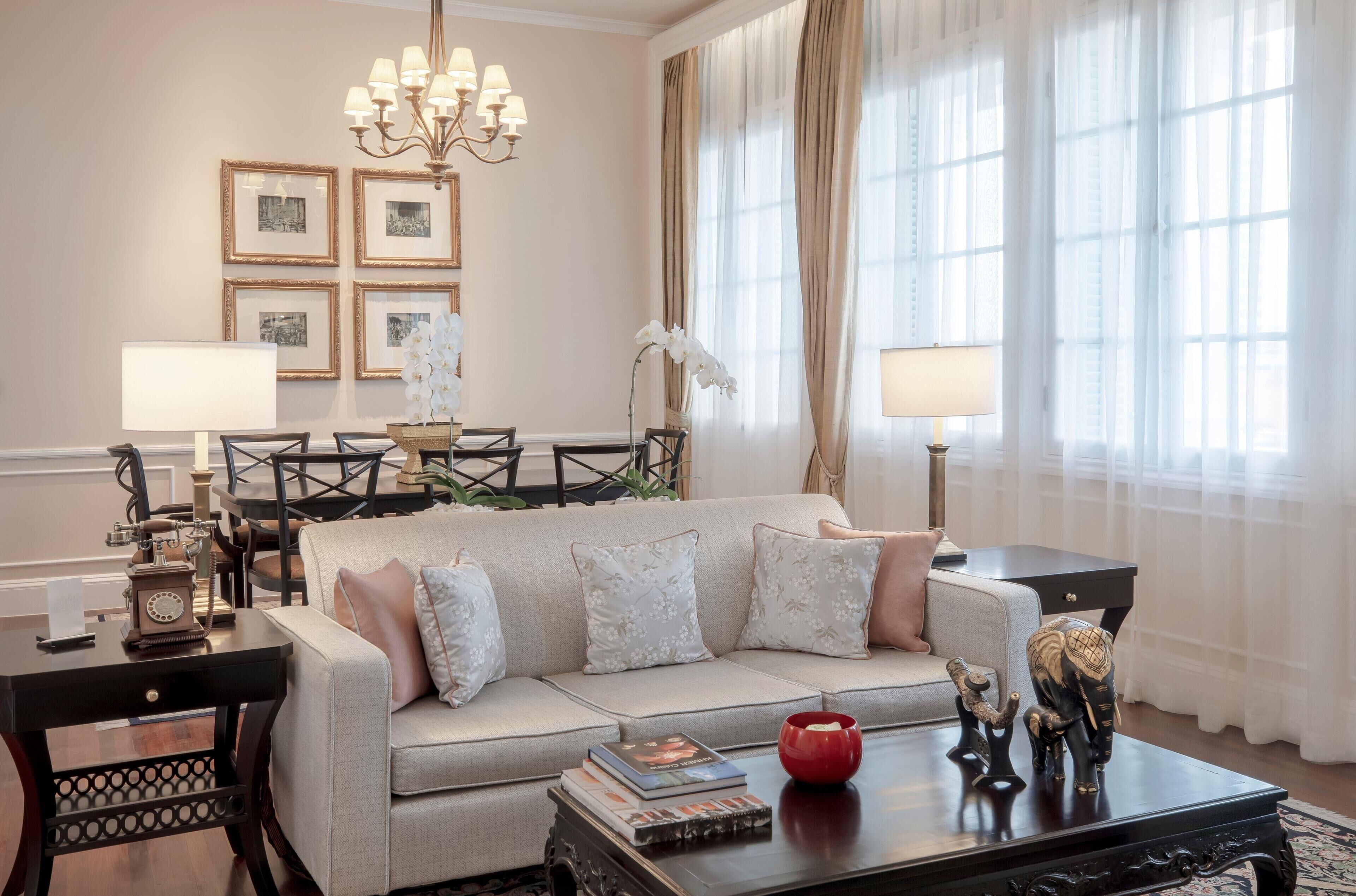 Una sala de estar con sofá, mesa de centro y candelabro. Se observan cuadros en la pared y una lámpara en la mesita auxiliar.