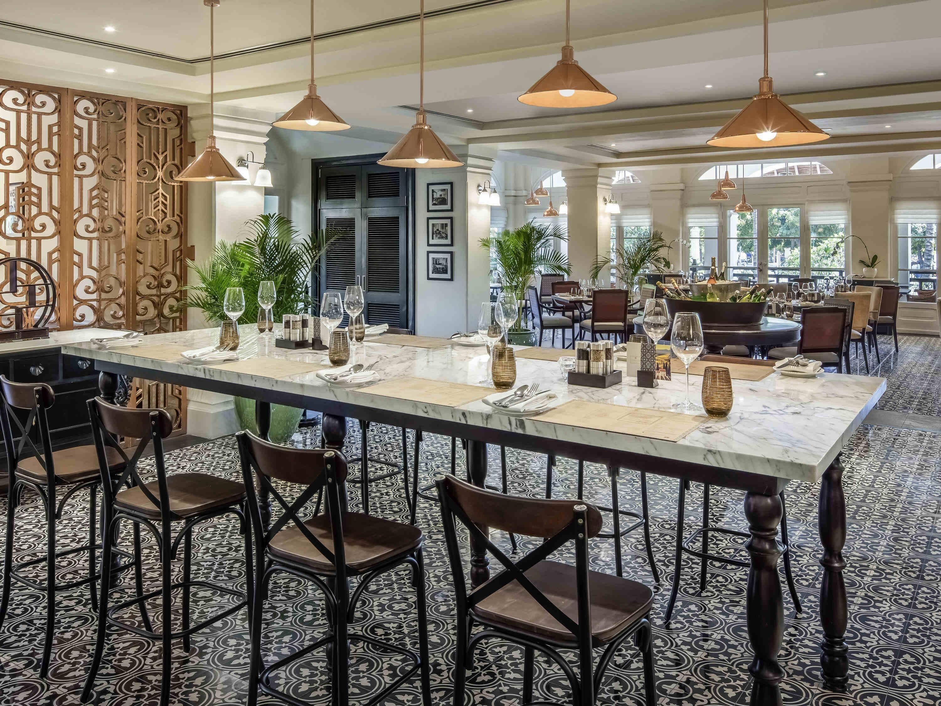 Un comedor amplio con una mesa larga, numerosas sillas, lámparas colgantes y un separador decorativo.