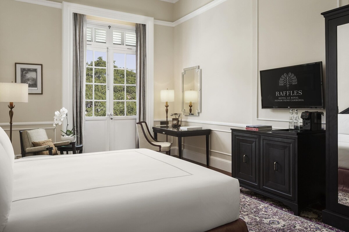 A hotel room with a bed, a desk, a chair, a television, and a window with curtains.