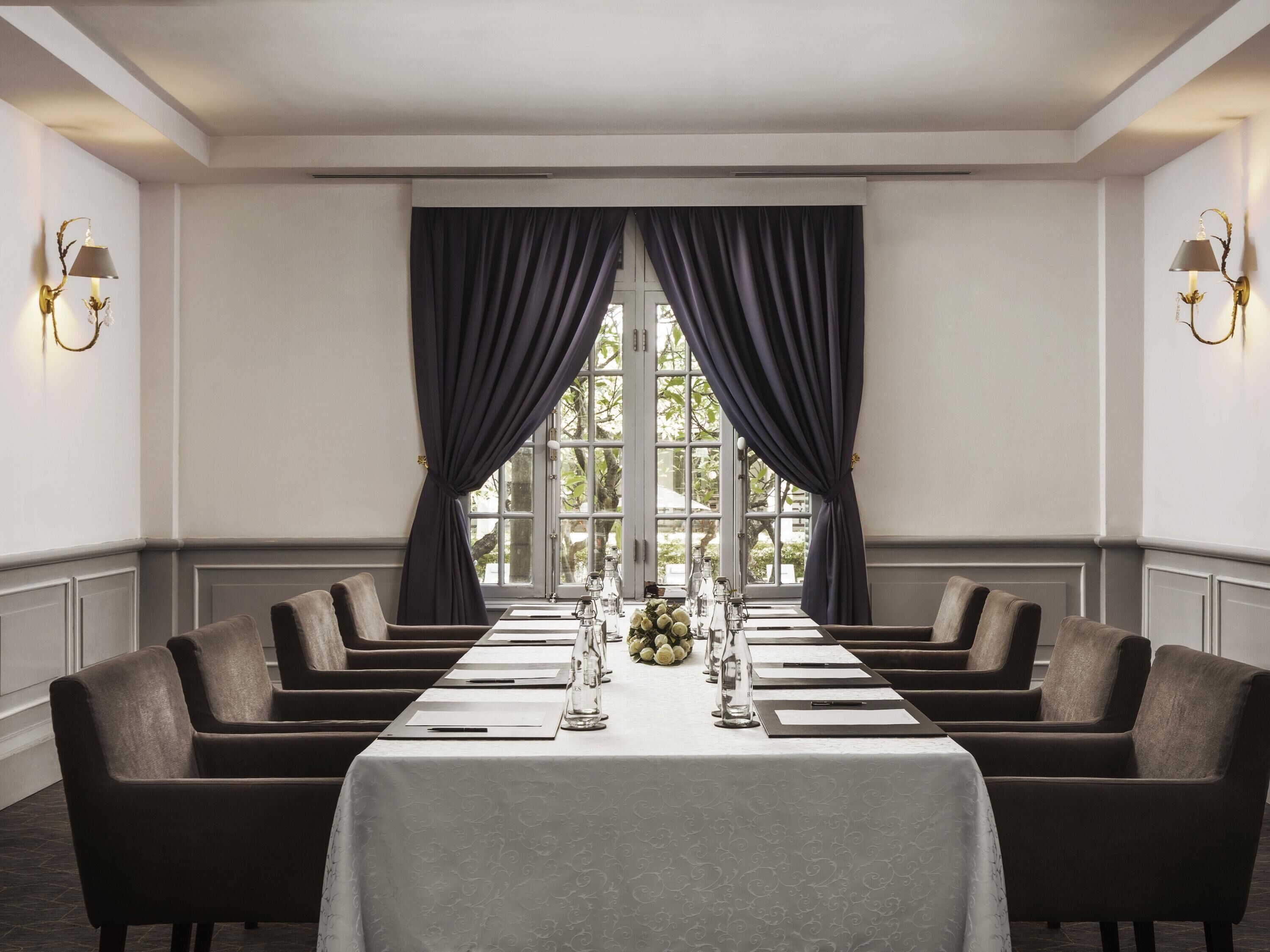 A conference room with a long table, dark curtains, and wall-mounted lamps.
