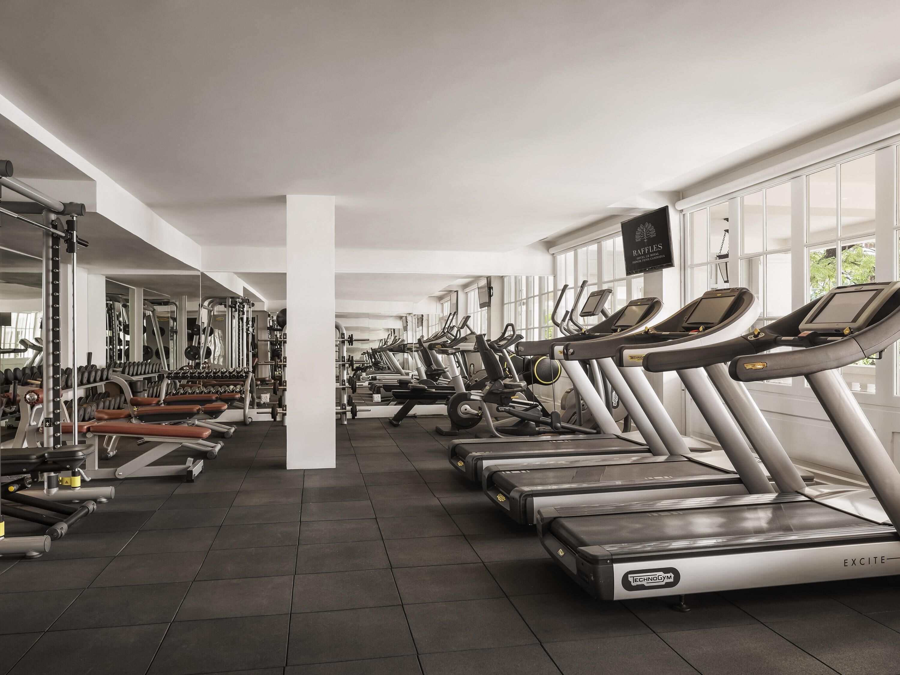 Een fitnessruimte met loopbanden, krachttrainingsapparatuur en spiegels.