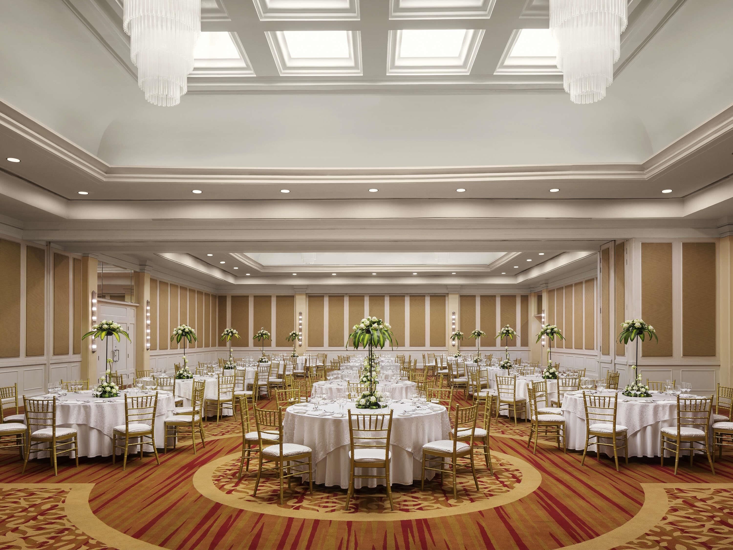 A large banquet hall with round tables, gold chairs, and floral centerpieces.