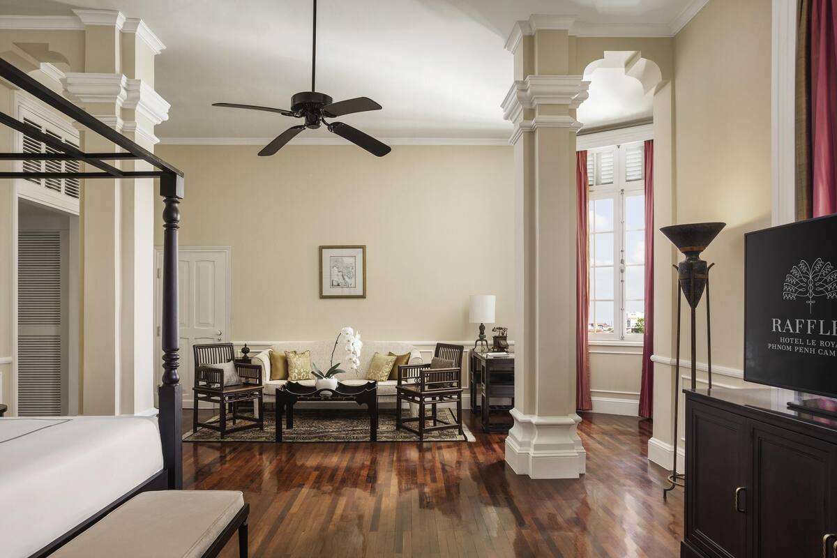 A hotel room with a wooden floor, a ceiling fan, a sofa, a coffee table, and a TV.