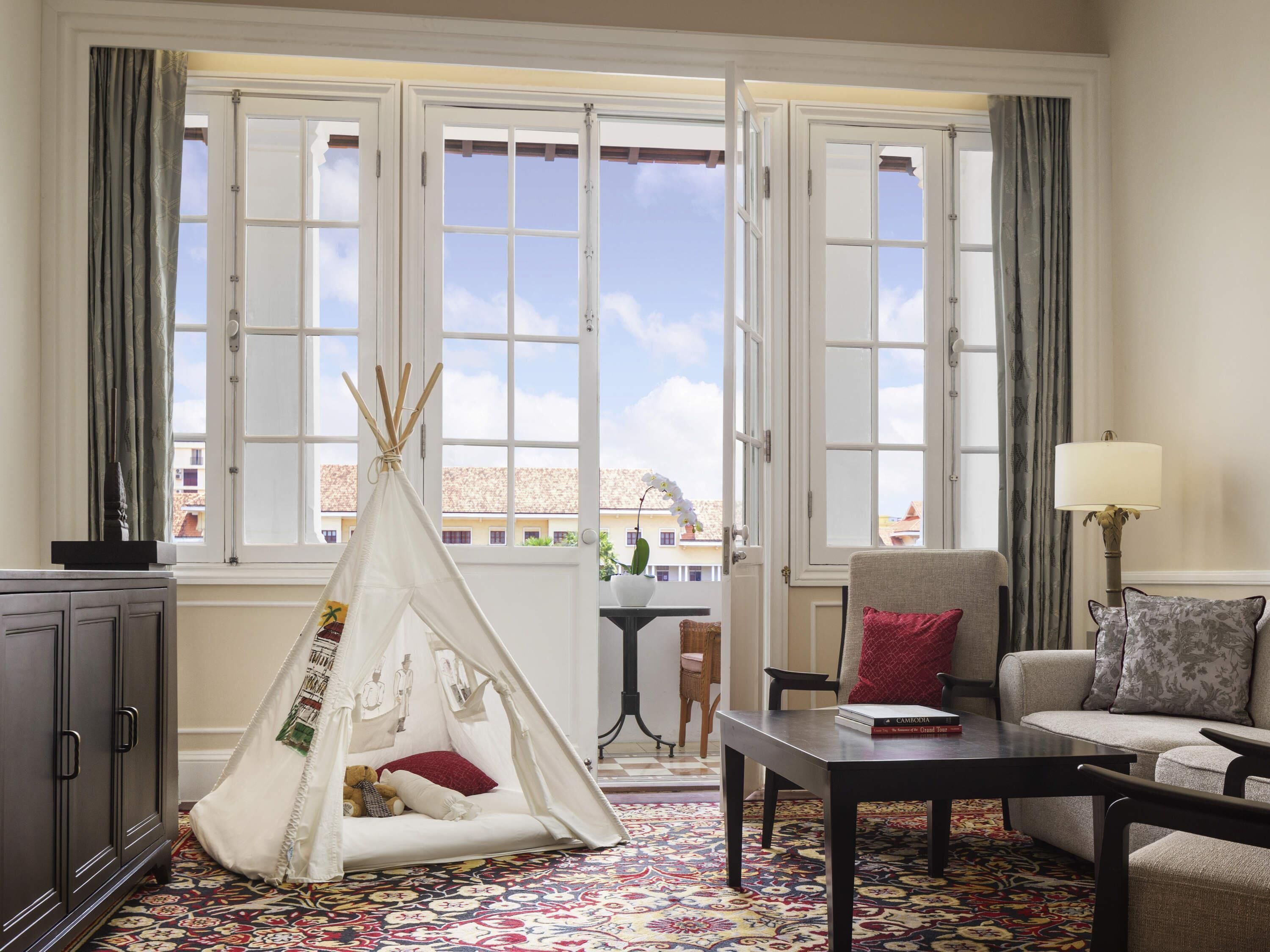 A room with a large window, a sofa, a table, a lamp, a chair, a cabinet, and a decorative tent.