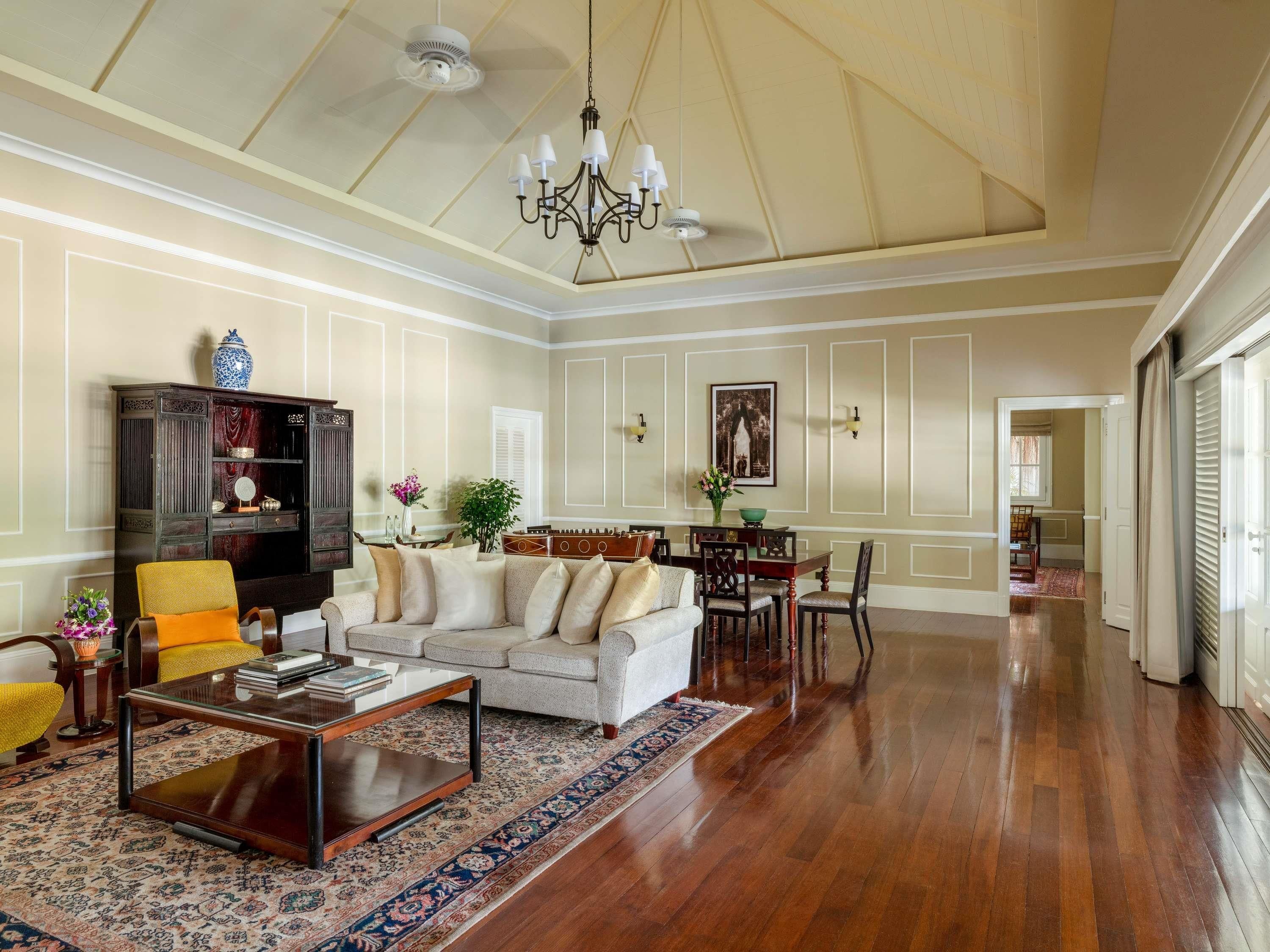 A spacious living room with a high ceiling, a chandelier, a sofa set, a coffee table, and a dining area with chairs and a table.