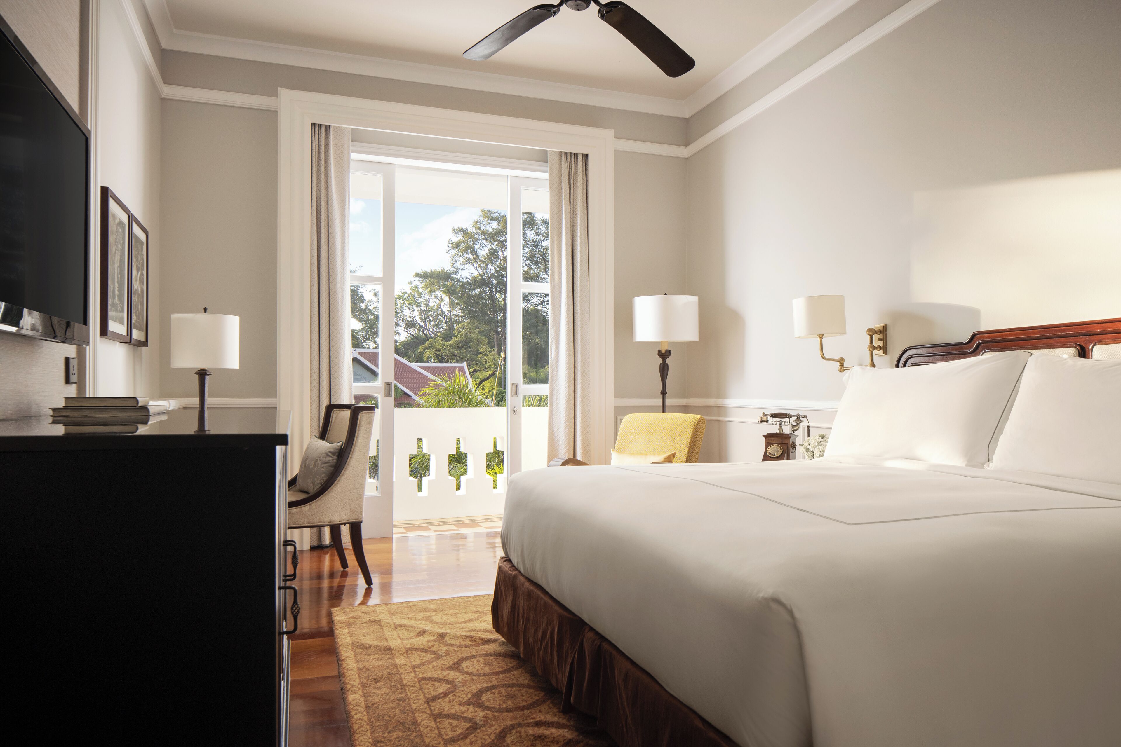 A hotel room with a large bed, a desk, a chair, and a view of the outdoors through a sliding door.