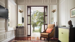 A room with a television, a patterned rug, a chair, a cabinet, and a view of palm trees through a door.