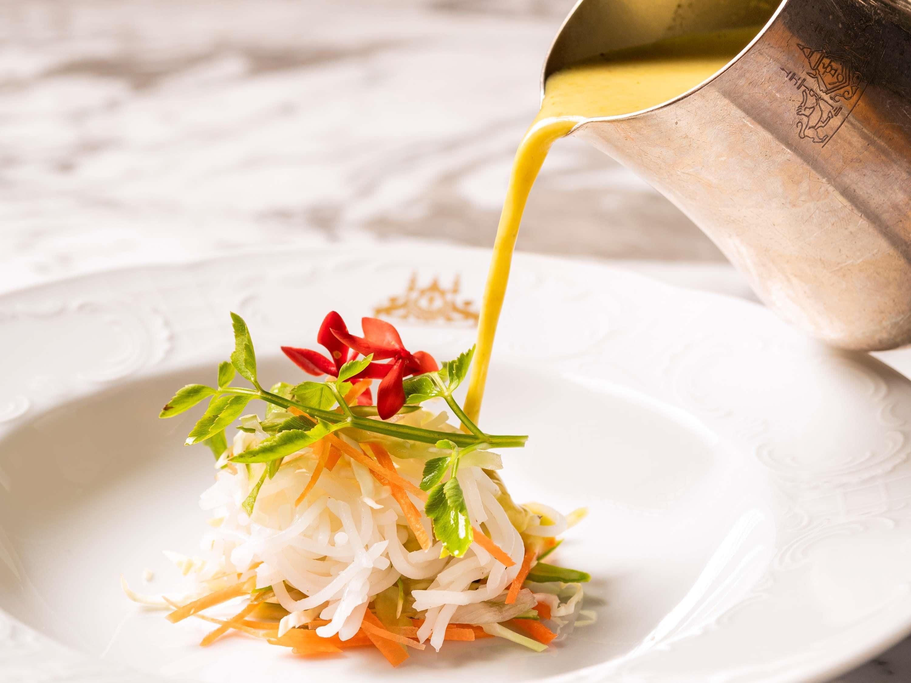 A dish with shredded vegetables and a red flower, being poured from a metal pitcher.