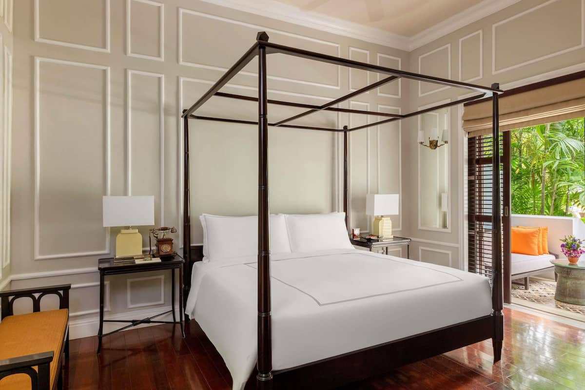 A four-poster bed in a room with a view of greenery outside.