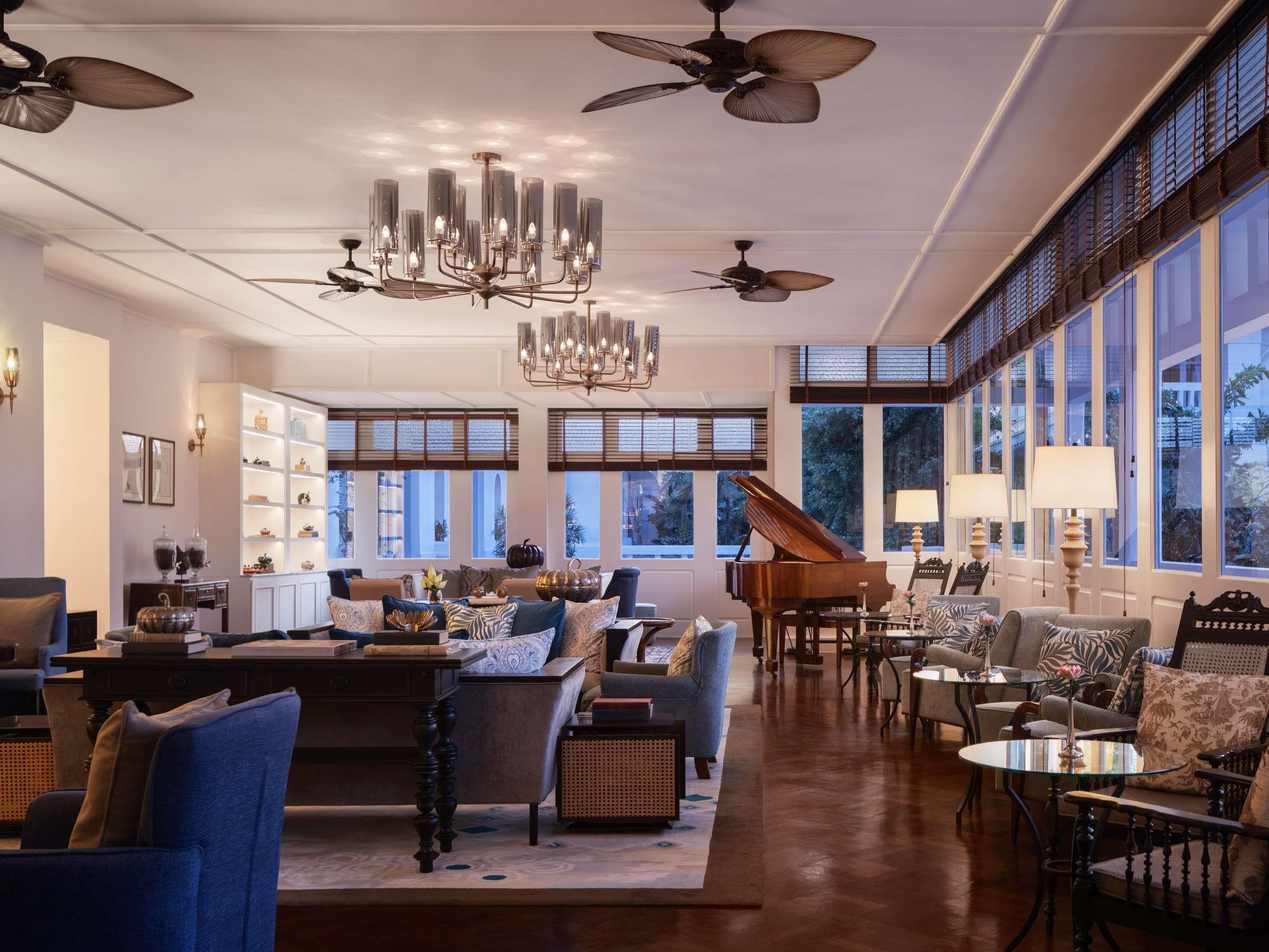 A spacious living room with a grand piano, multiple seating areas, and large windows offering natural light.