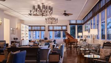 A spacious living room with a grand piano, multiple seating areas, and large windows offering natural light.