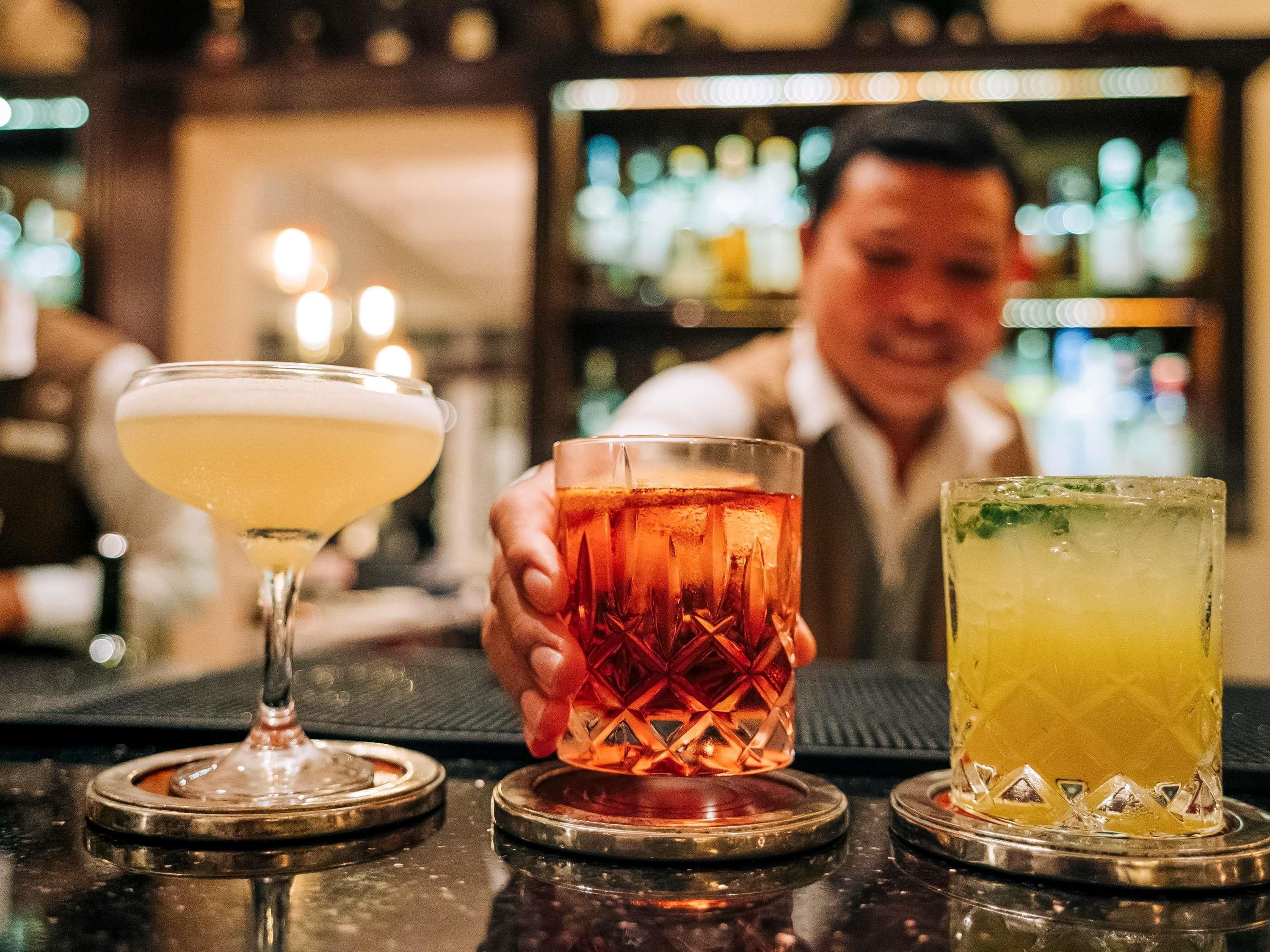 Drie verschillende soorten drankjes op een barkruk met een vage achtergrond van een bar.